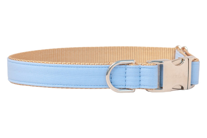 Minimalist light blue dog collar with a soft-textured cotton exterior, tan webbed interior for durability, and shiny silver metal fittings for secure leash attachment and closure.