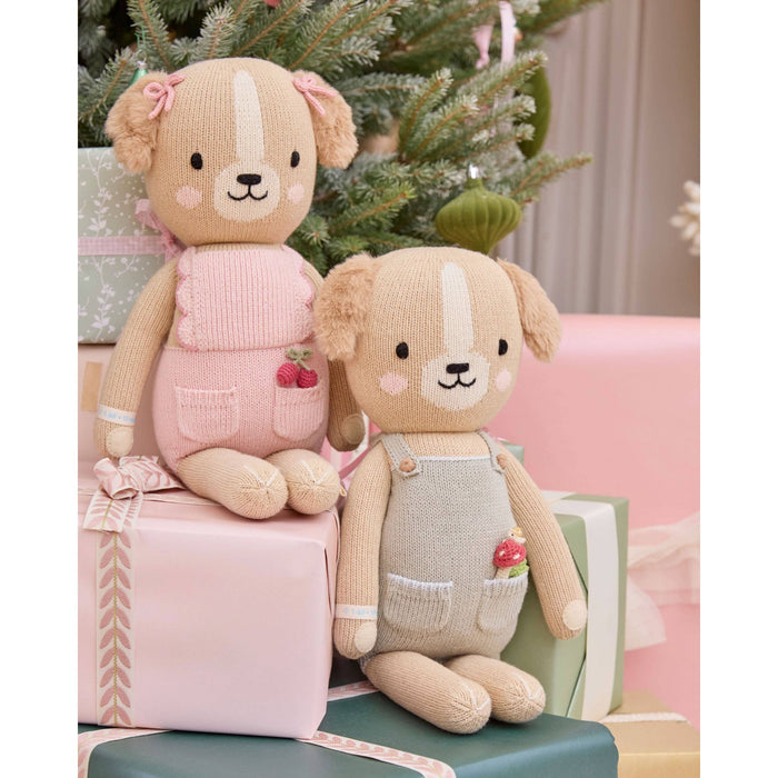 Two knitted teddy bears sitting on presents with a Christmas tree in the background