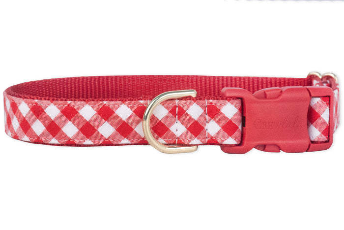 Classic red plaid dog collar featuring a checkered fabric overlay and reinforced red nylon backing. The collar has a red p[lastic buckle for secure closure and a D-ring for leash or accessory attachment.