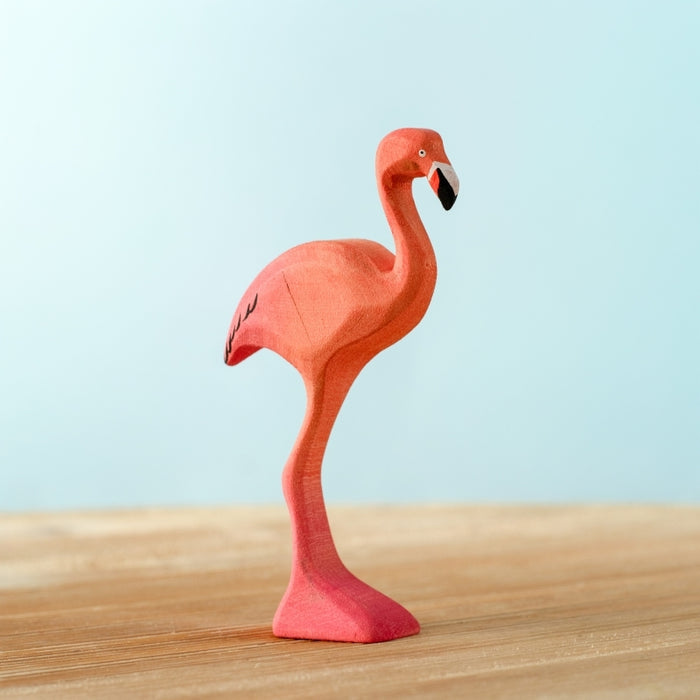 Plush flamingo toy on a wooden surface with a light blue background