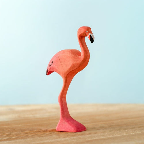 Plush flamingo toy on a wooden surface with a light blue background
