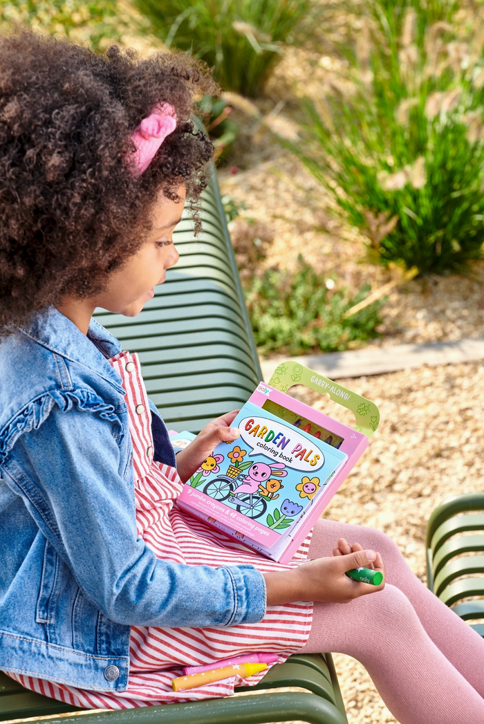 Child holding a pink tablet with 'Garden Pals' on the screen, sitting outdoors.