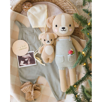 Baby outfit with teddy bear, hat, and green overalls on a textured surface with Christmas decorations.