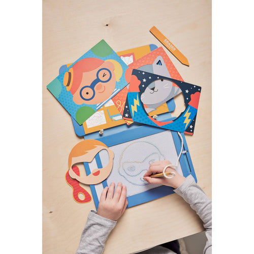 Child drawing with colorful paper cutouts of faces on a wooden table