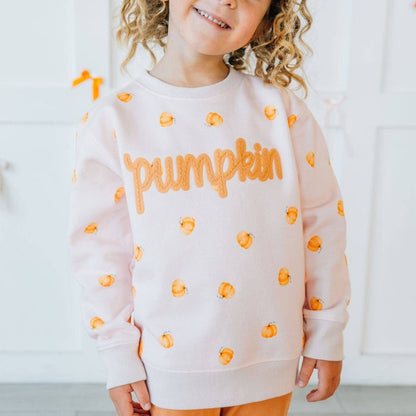 Child wearing a white sweatshirt with orange 'Pumpkin' text and pumpkin patterns on a light background