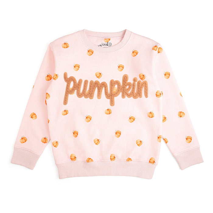A light pink crewneck sweatshirt featuring the word 'pumpkin' in textured orange letters across the chest, surrounded by small orange pumpkin prints, laid flat on a white background.