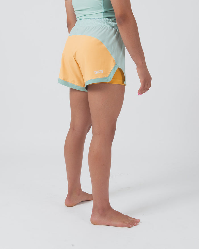 Kingz Hybrid Women's Shorts Terra Green - Full Body Right Side Profile Female Athlete Two-Tone Color Block Mint Green Front Panel Golden Yellow Back Panel KINGZ Text Badge Front Competition Cut Women's Grappling Shorts No-Gi BJJ [color:Light Green]