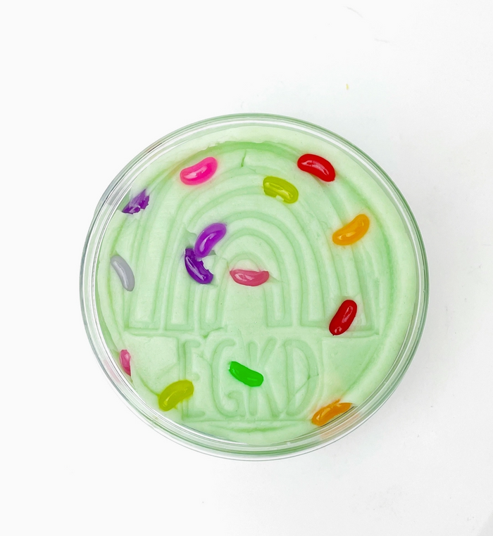 Green slushie with colorful jelly beans in a transparent cup on a white background