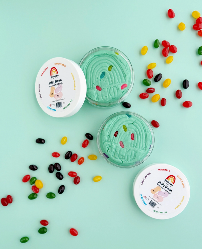 Green jelly bean ice cream in a container with scattered jelly beans on a light blue background