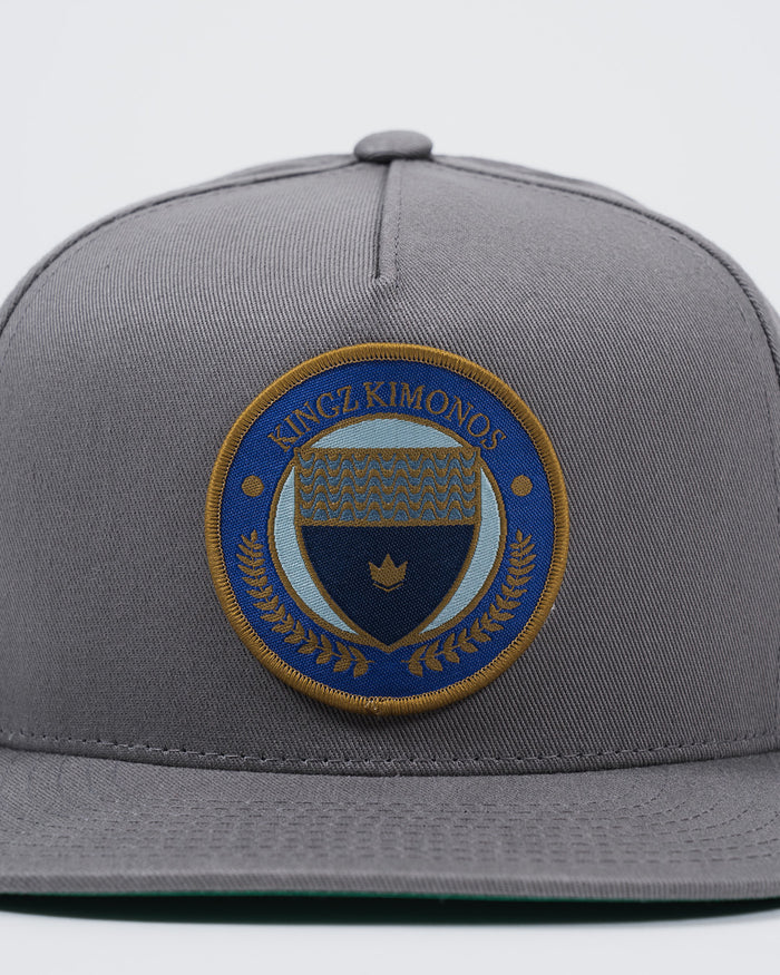 Kingz Jiu Jitsu Club Snapback Grey - Close-Up Front View Embroidered Kingz Kimonos Circular Patch Blue Gold Crown Laurel Detail Structured Fit BJJ Hat [color:Grey]