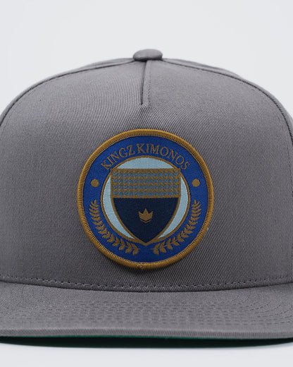 Kingz Jiu Jitsu Club Snapback Grey - Close-Up Front View Embroidered Kingz Kimonos Circular Patch Blue Gold Crown Laurel Detail Structured Fit BJJ Hat [color:Grey]