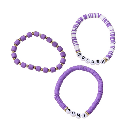 Three purple beaded bracelets with name beads on a beige surface.