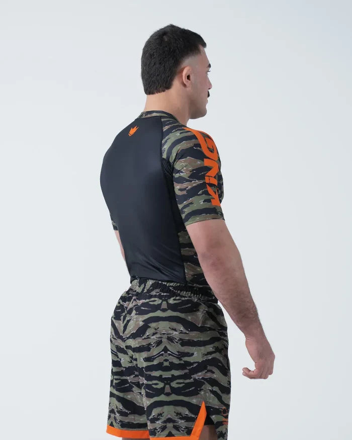 Kingz Always Hunting Rashguard Green Camo - Full Body 3/4 Back View Right Side Male Athlete Short Sleeve Tiger Camo Orange Crown Logo Black Back Panel Camo Shorts Orange Stripe [color:Green Camo]