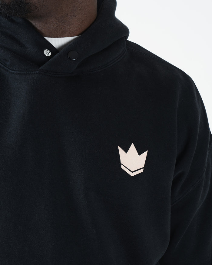 Black BJJ hoodie chest detail closeup of tan crown logo with snap button collar and dual panel neckline [color:Black]