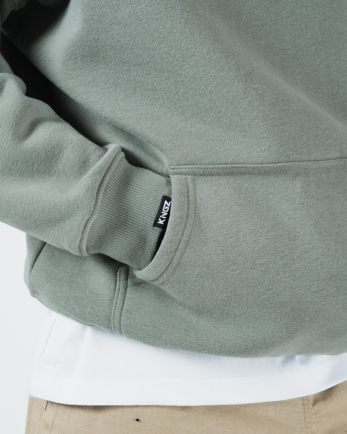 Dark forest green BJJ hoodie hem detail closeup showing woven Kingz label ribbed cuff and pocket edge