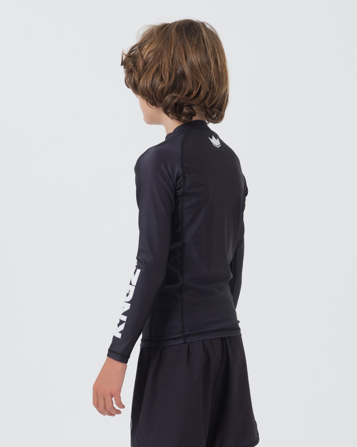 Kingz Kore V2 Youth L/S Rashguard Navy Black - Full Body Right Side Profile View Teen Boy Athlete Long Sleeve Navy Blue Crown Logo Circle Left Chest KINGZ White Vertical Right Sleeve Text Matching Navy Shorts Kids BJJ [color:Black]