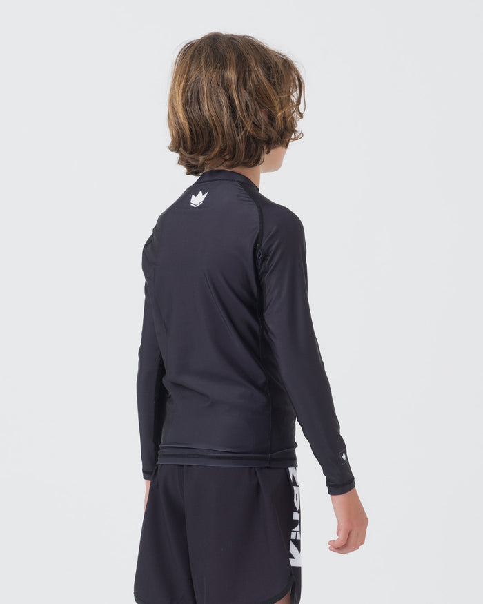 Kingz Kore V2 Youth L/S Rashguard Navy Black - Full Body 3/4 Back Left Side View Teen Boy Athlete Long Sleeve Navy Blue Crown Logo Upper Back Center Matching Navy Shorts KINGZ White Side Text Kore V2 Kids BJJ Training [color:Black]