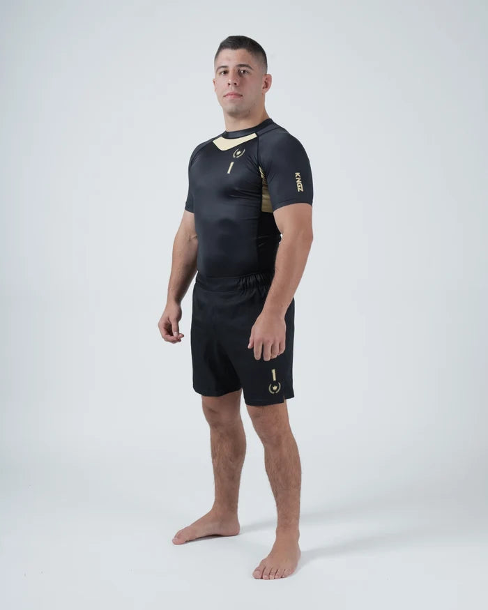Kingz Player Special Limited Edition Rashguard Black Gold - Full Body 3/4 Angled Front View Barefoot Male Athlete Short Sleeve Gold Chevron Diagonal Panel KINGZ Text Sleeve Shorts [color:Black]