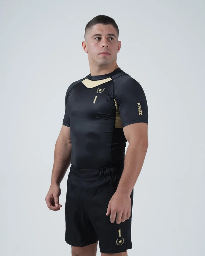 Kingz Player Special Limited Edition Rashguard Black Gold - Full Body Back View Right Side Barefoot Male Athlete Gold Center Back Panel Winged Crown Logo Black Shorts KINGZ Text [color:Black]