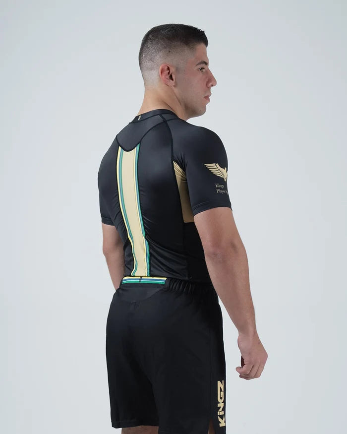 Kingz Player Special Limited Edition Rashguard Black Gold - Full Body Back View Male Athlete Short Sleeve Lotus JPS Inspired Gold Center Back Stripe Teal Border Black Spats Shorts [color:Black]