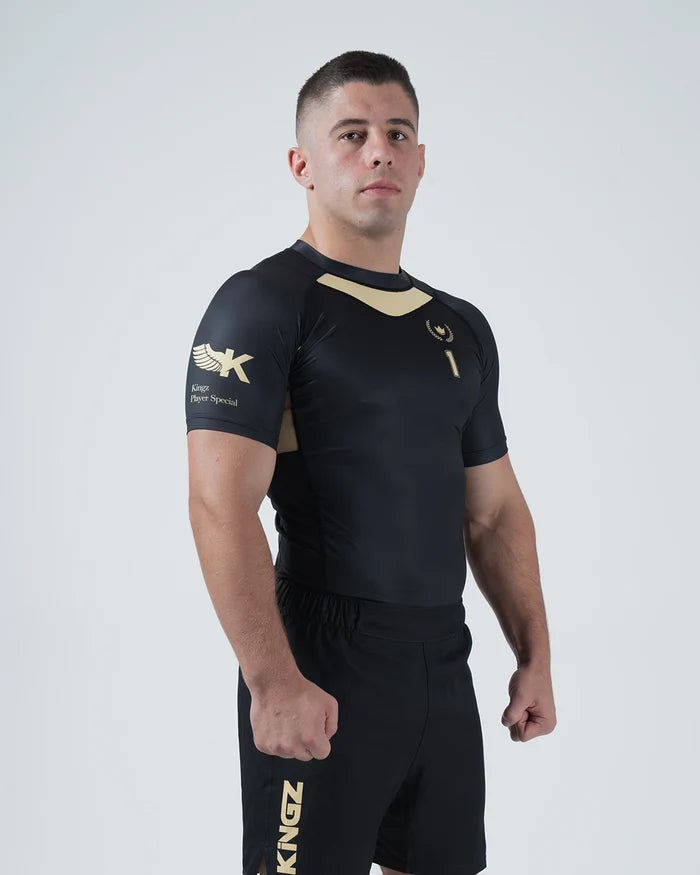 Kingz Player Special Limited Edition Rashguard Black Gold - Full Body 3/4 Angled Front View Male Athlete Short Sleeve Gold Chevron Chest Panel Number 1 Winged K Logo KINGZ Gold Text Shorts [color:Black]