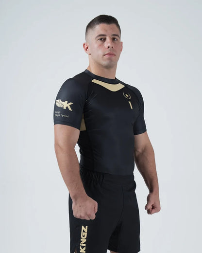 Kingz Player Special Limited Edition Rashguard Black Gold - Full Body 3/4 Angled Front View Male Athlete Short Sleeve Gold Chevron Chest Panel Number 1 Winged K Logo KINGZ Gold Text Shorts [color:Black]