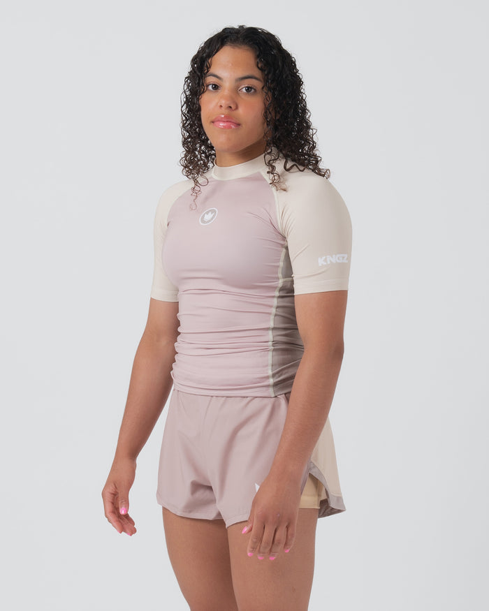 Kingz Terra Women's Rashguard Soil Edition - Full Body 3/4 Front Left Side View Female Athlete Short Sleeve Dusty Rose Mauve Body Cream Beige Raglan Sleeves Crown Logo Circle KINGZ Right Sleeve Text Matching Mauve Hybrid Shorts Women's BJJ [color:Baby Pink]