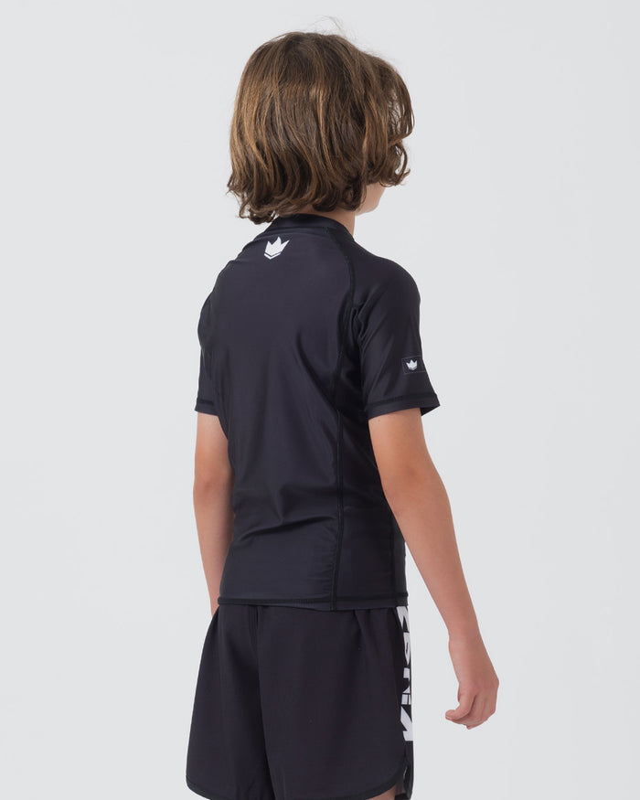 Kingz Kore V2 Youth S/S Rashguard Navy Black - Full Body 3/4 Back View Teen Boy Athlete Short Sleeve Navy Blue Crown Logo Upper Back KINGZ White Sleeve Text Visible Navy Shorts Kore V2 Kids Youth BJJ Guard Sublimated [color:Black]