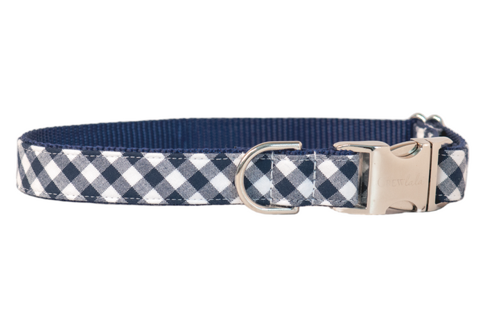 Classic navy plaid check dog collar with durable stitching and a blue webbed interior. Includes a curved metal buckle for quick fastening and a matching D-ring for tags or leash connection.