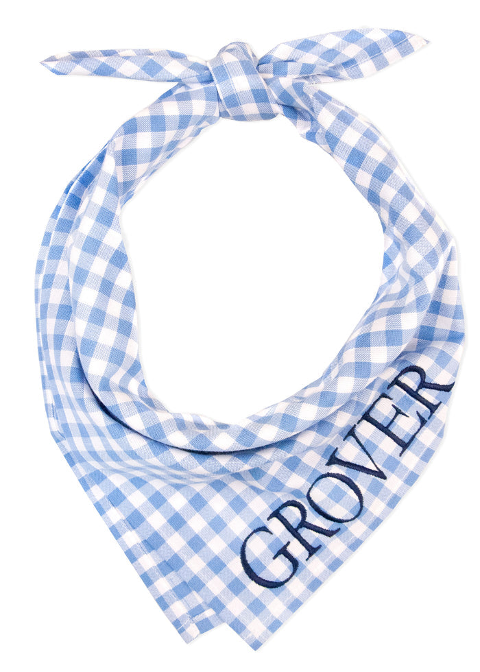 Personalized dog bandana made from soft cotton in a periwinkle plaid pattern, tied in a simple knot. The name “GROVER” is embroidered diagonally in bold navy thread near the bottom tip, standing out against the checkered background.