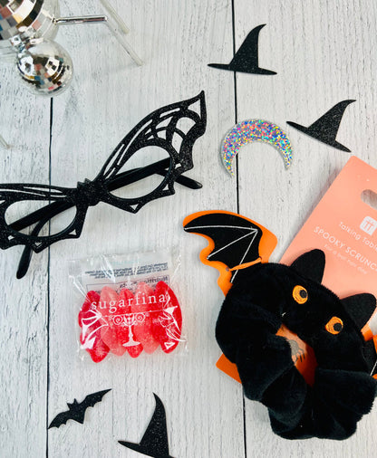 Halloween-themed items including a black spider web, red gummy worms, and a black bat toy on a wooden surface.