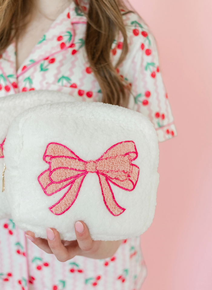 Person holding a plush toy with a pink bow against a pink background