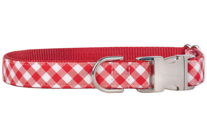 Classic red plaid dog collar featuring a checkered fabric overlay and reinforced red nylon backing. The collar has a shiny metal buckle for secure closure and a D-ring for leash or accessory attachment.