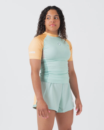 Kingz Terra Women's Rashguard Green Edition - Full Body 3/4 Front Right Side View Female Athlete Short Sleeve Mint Green Body Yellow Peach Raglan Sleeves Crown Logo KINGZ White Left Sleeve Text Matching Mint Hybrid Shorts Terra Collection BJJ [color:Light Green]