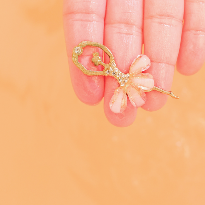 Gold and pink decorative item held between fingers against a peach background
