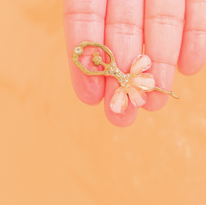 Gold and pink decorative item held between fingers against a peach background